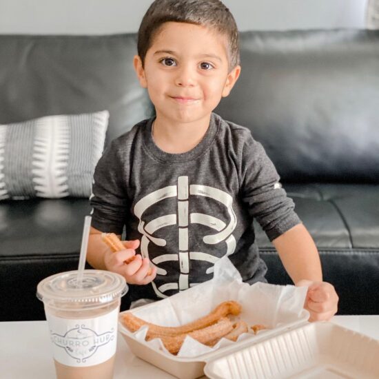 Young boy eating churros on a couch.