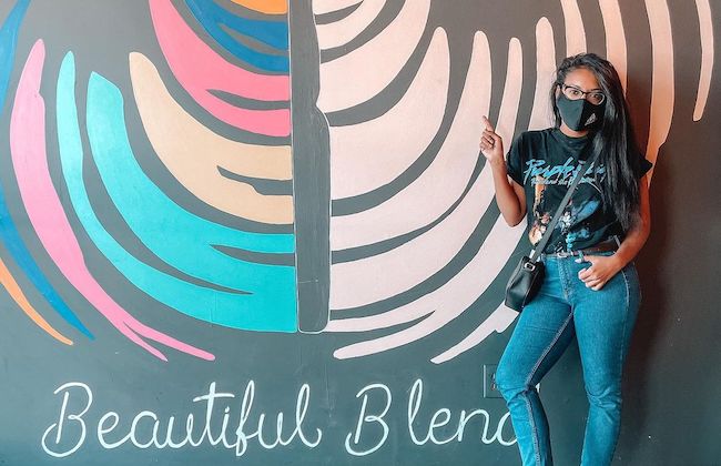 Woman in face mask standing by colorful wall.